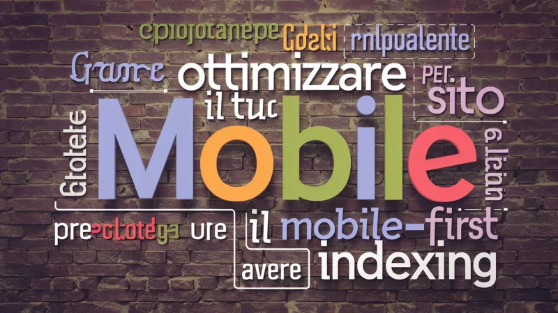 Una nuvola di parole su un muro di mattoni testurizzato con parole come "ottimizzare", "Mobile", "sito", "mobile-first indexing", in vari colori e font. Il testo è in italiano, e sottolinea l'ottimizzazione mobile.